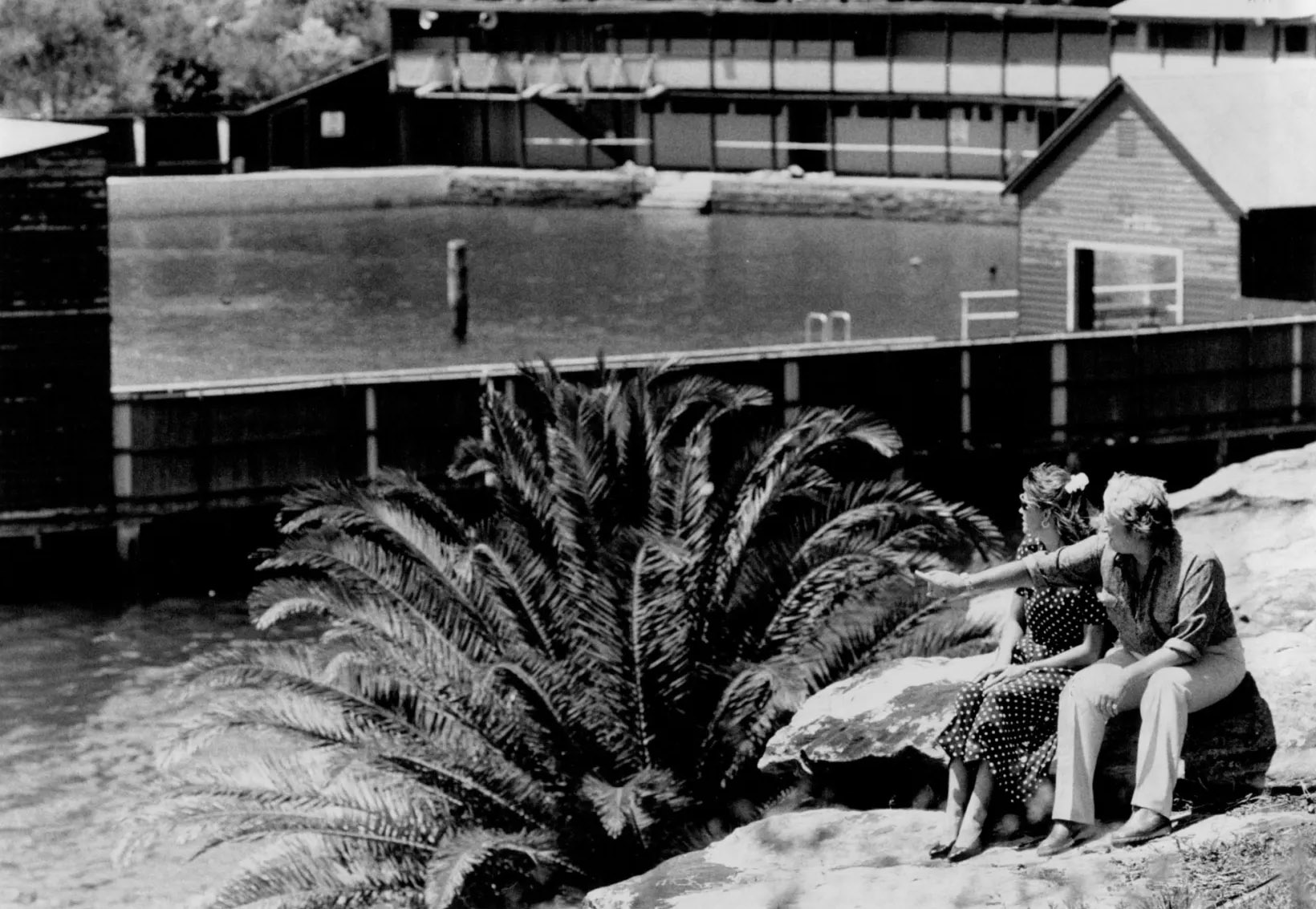 Black and white photo of Dawn Fraser and Shelley Taylor-Smith sitting on the cliffs at sunny white horse point, with the pool in the background