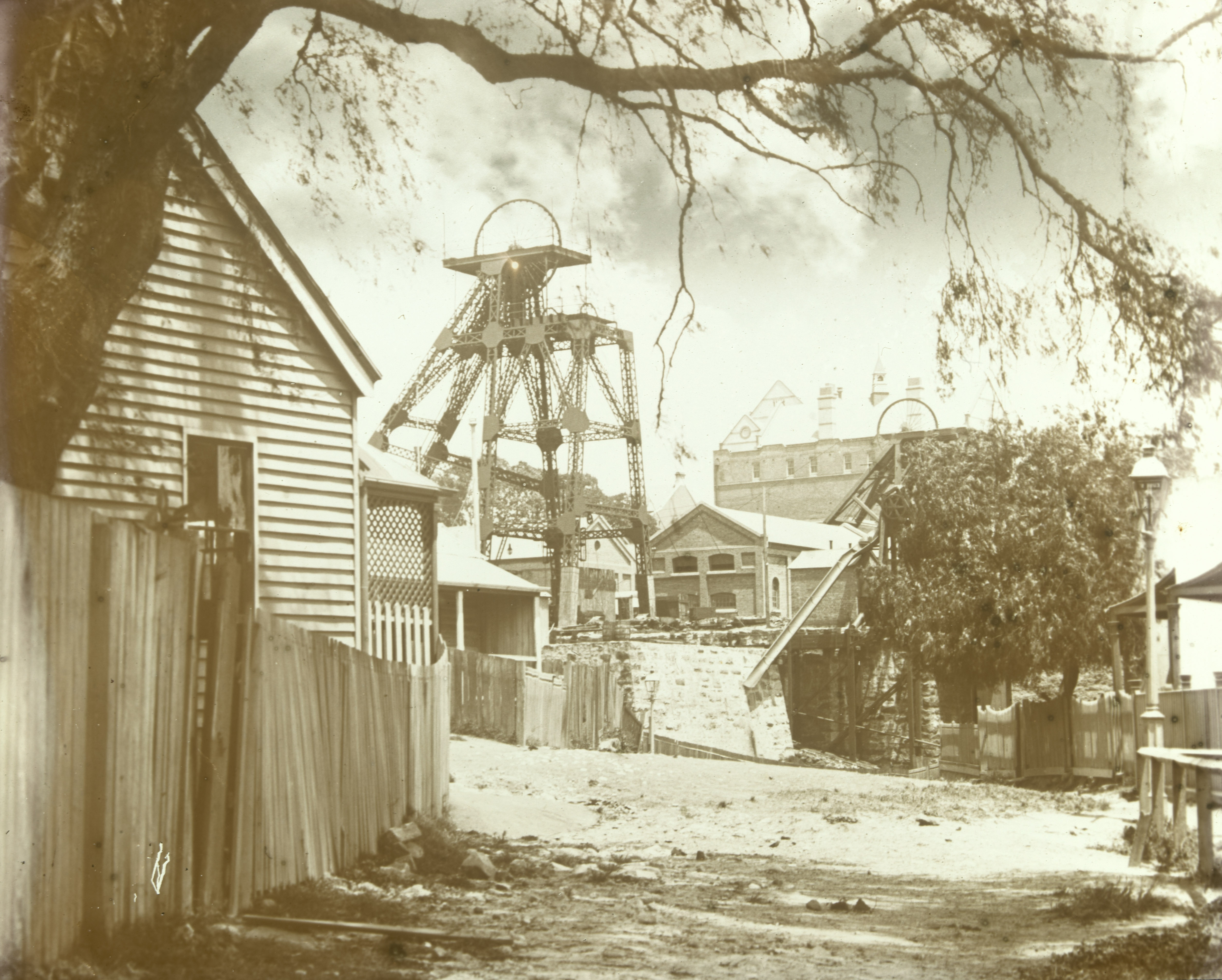 Sepia image of the Balmain colliery mining tower surrounded by sandstone factory buildings along a dirt pathway